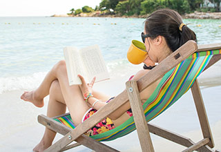 picture of woman drinking coffee and reading a book on the shore