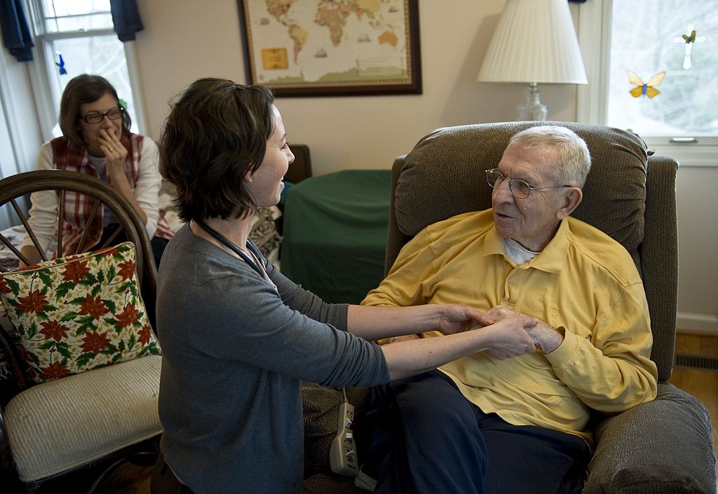 A hospice clinician checks on a patient at home, with a family member nearby.