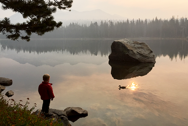 picture of young child looking at a lake amid a smoky sky 