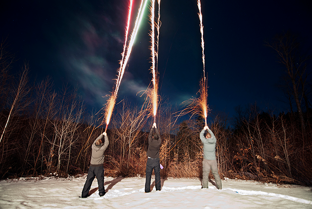 picture of three boys shooting mortar-type fireworks into the night sky 