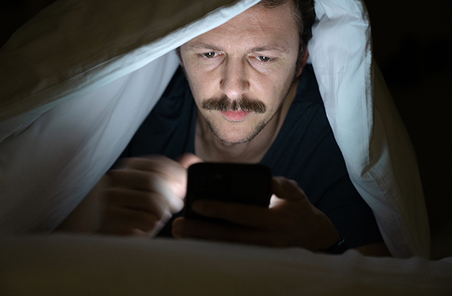picture of man looking at phone in bed at night