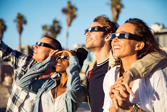 Four people looking upward at an eclipse with protective glasses.