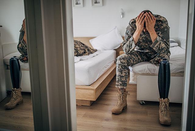 A soldier sits on a bed with his head in his hands.