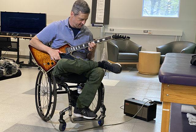 A man in a wheelchair strums guitar.