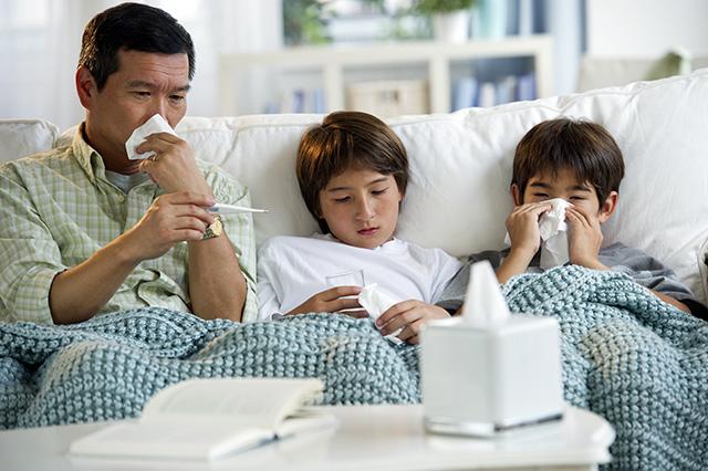 A father and his two sons sitting on a couch all have a respiratory illness