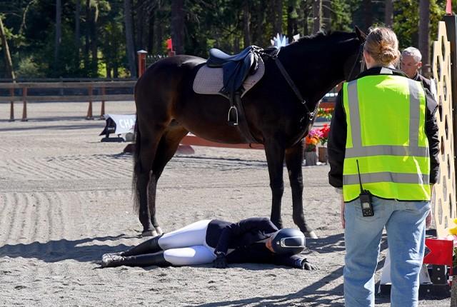 picture of a woman lying on the ground beside a horse in an arena