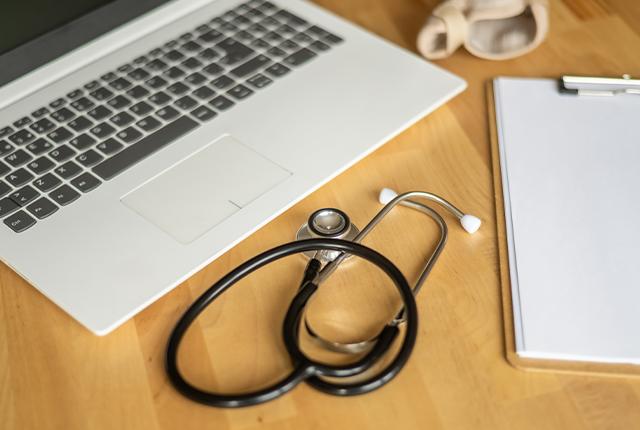 A laptop computer, stethoscope and notepad sit on a desk