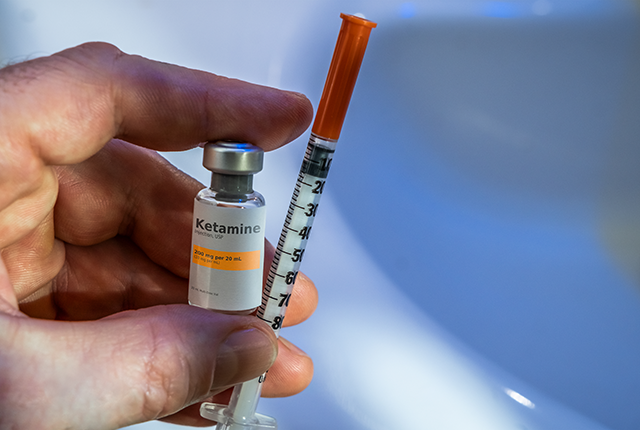 picture of a hand holding a vial of ketamine liquid and a syringe