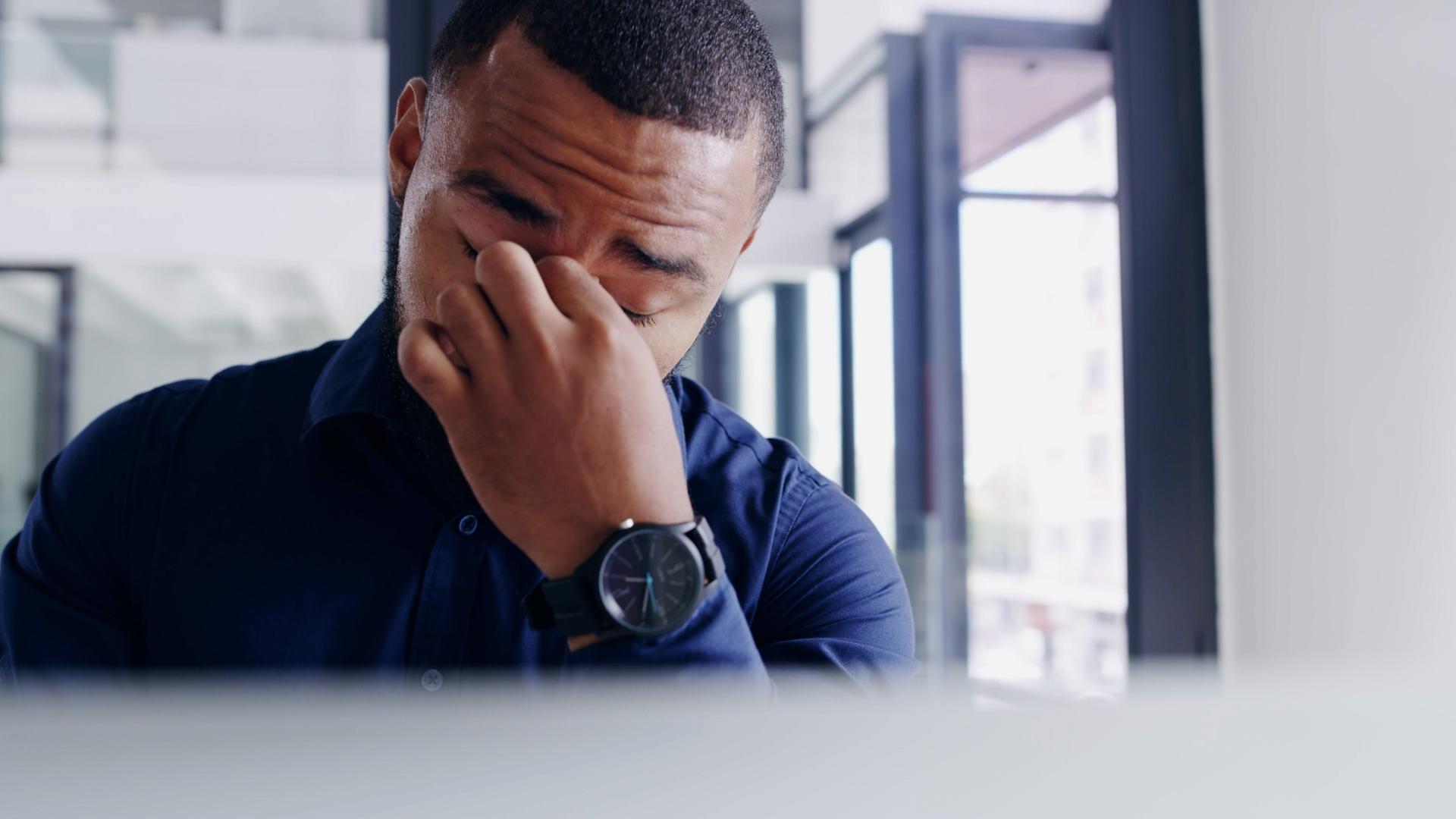 A man rubbing his eyes in an office.