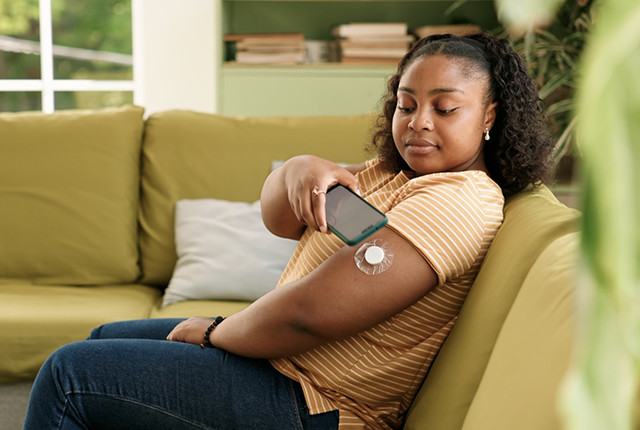 picture of woman sitting on sofa and getting a blood glucose reading for type 1 diabetes