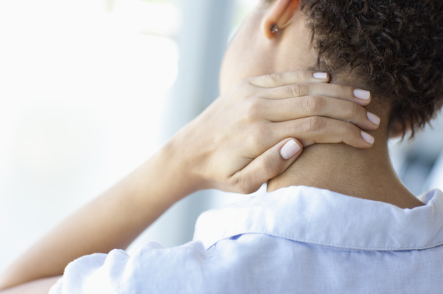 A woman holds the back of her neck with her hand.