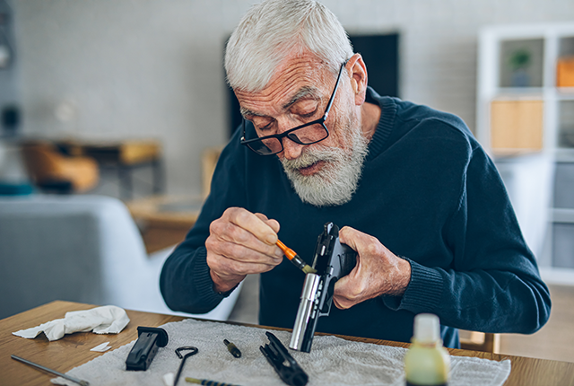 older man cleans a firearm at home
