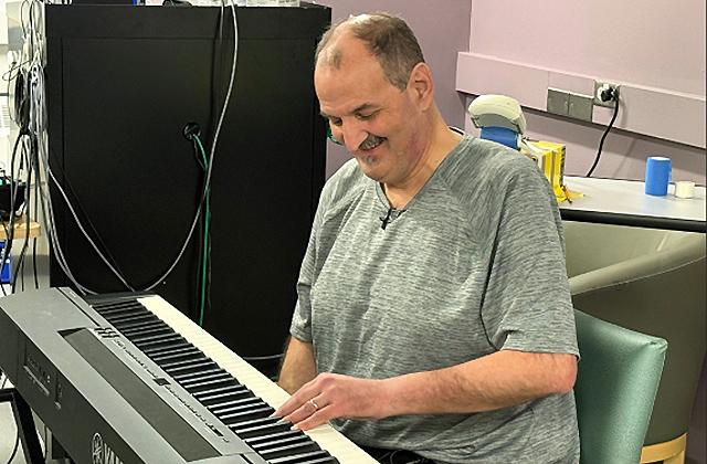 A man seated at a piano keyboard plays music with his left hand.