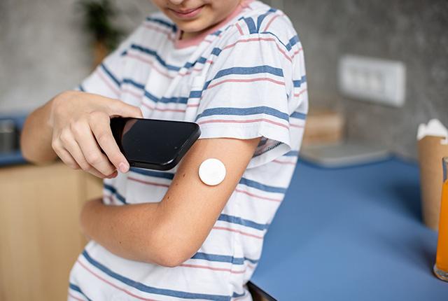 A child uses a smartphone to check blood sugar with a continuous glucose monitor.