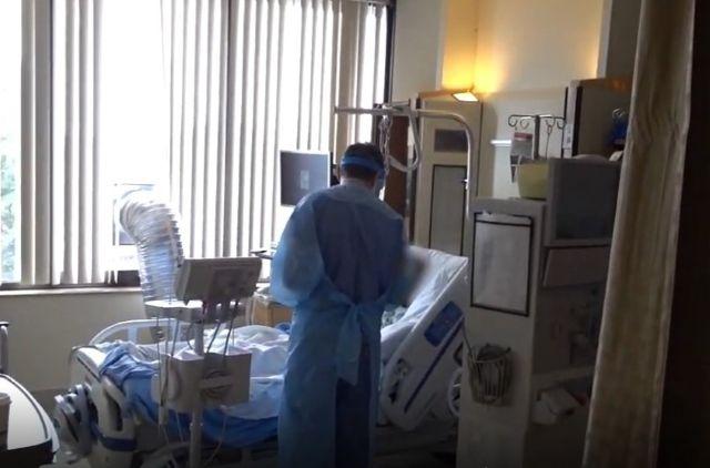 A healthcare worker in protective equipment works at the bedside of a COVID-19 patient in a hospital room.